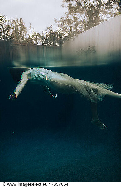 Woman body floating underwater in a care free vibe wearing dress