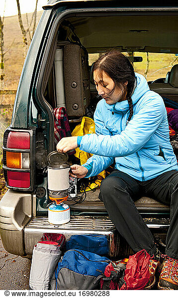 woman boiling water on camping stove at the back of her car
