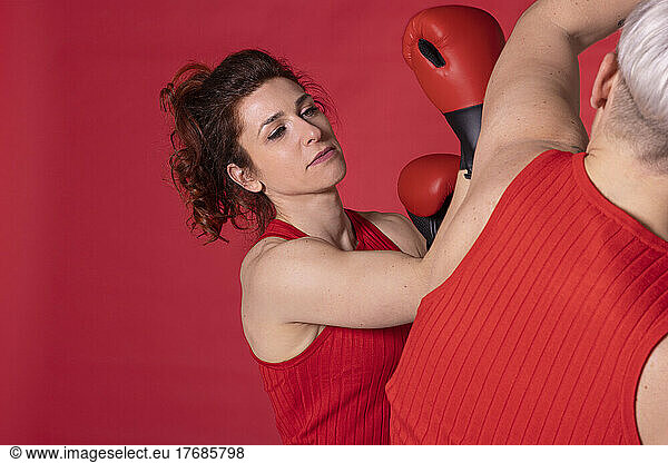 Woman boxing with friend against red background