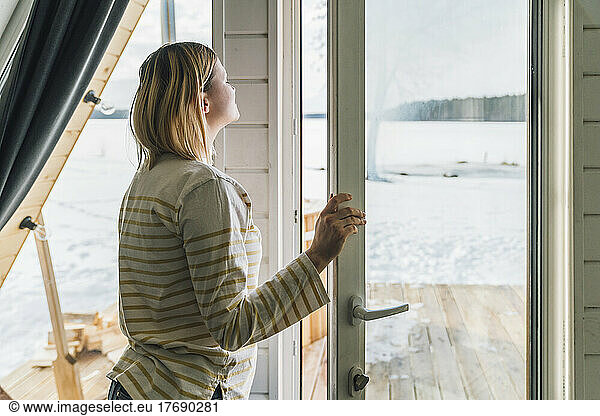 Woman breathing fresh air by glass door at home