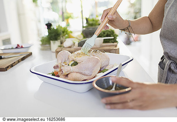 Woman brushing raw chicken with sauce in kitchen