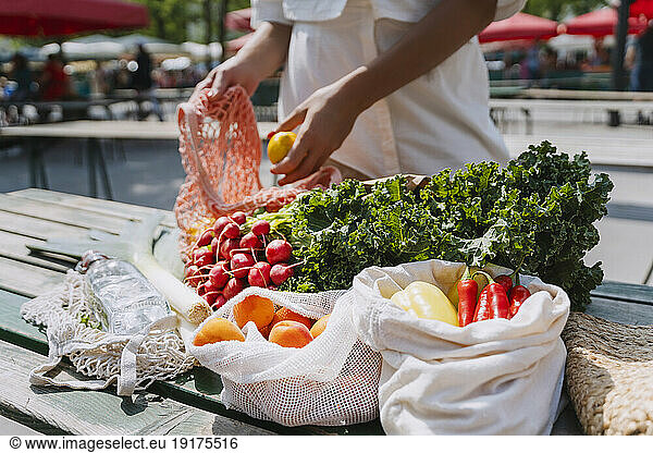 Woman buying fresh fruits and vegetables in market on sunny day