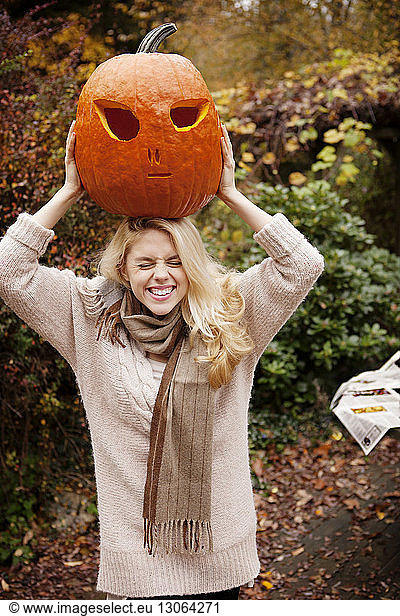 Woman carrying Halloween pumpkin on head while standing at backyard