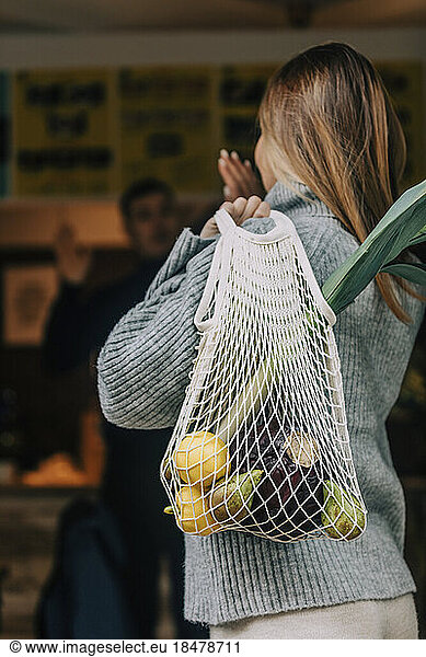 Woman carrying mesh bag with fruits and vegetables