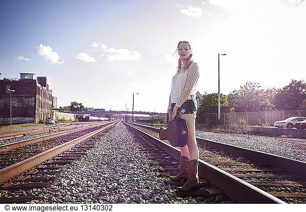 Woman carrying musical case while standing on railroad tracks