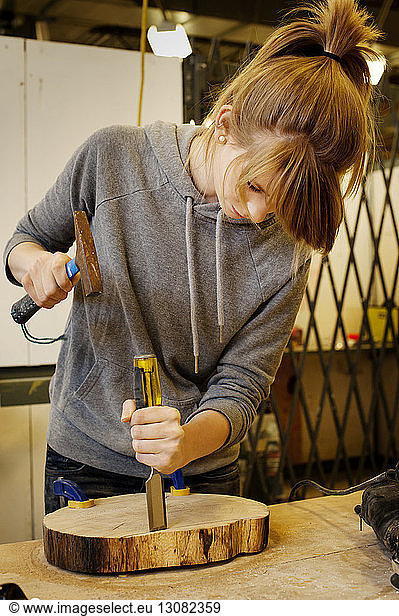 Woman carving wood by using chisel and hammer at workshop
