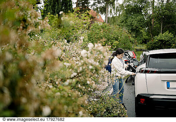 Woman charging electric car while standing by plants