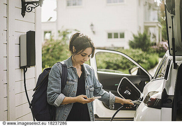 Woman charging electric car while using smart phone
