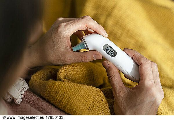 Woman checking temperature with thermometer at home