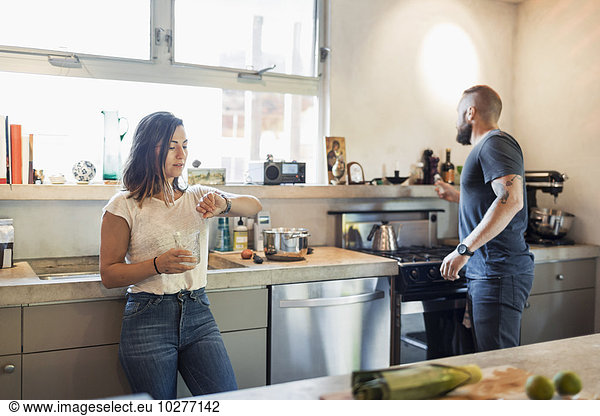 Woman checking time while man looking through window in kitchen