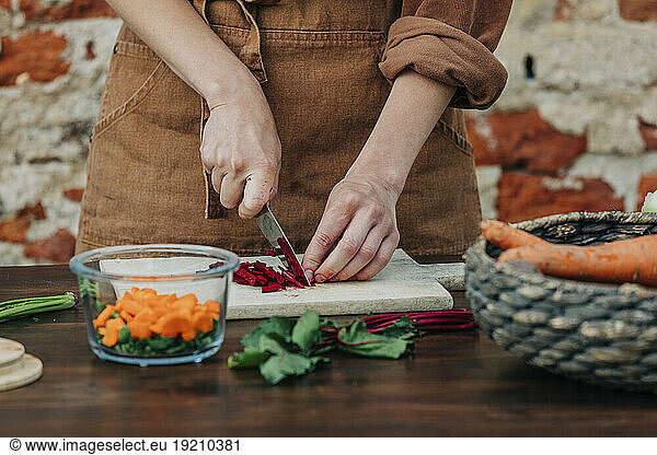 Woman chopping common beet on table in front of brick wall