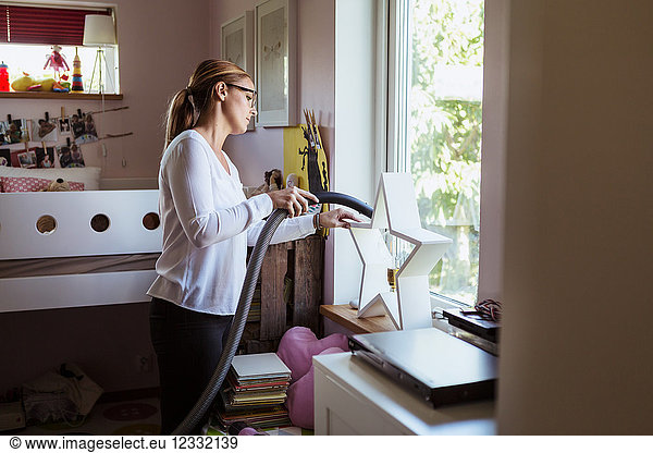 Woman cleaning bedroom with vacuum cleaner at home