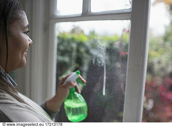 Woman cleaning windows with glass cleaner spray bottle