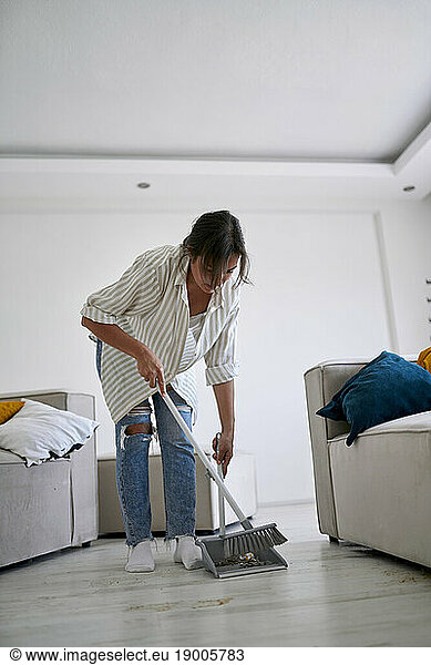 Woman cleaning with broom in living room at home