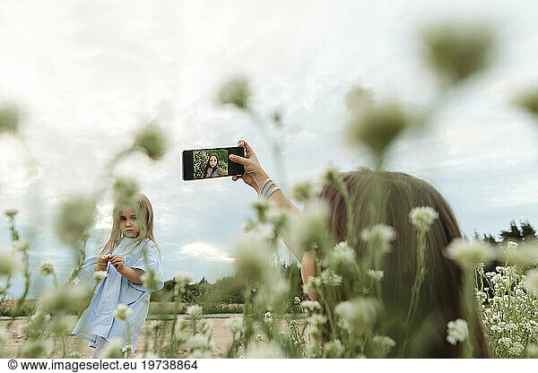 Woman clicking selfie through smart phone in front of girl standing at field