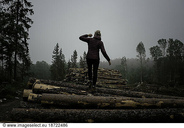 woman climbing a pile of logs in the forest
