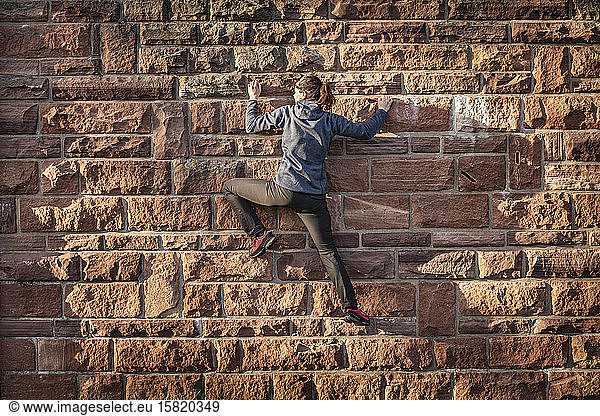 Woman climbing on sandstone brick wall