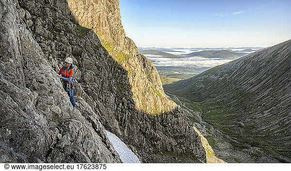 Woman climbing rocky mountain on sunny day