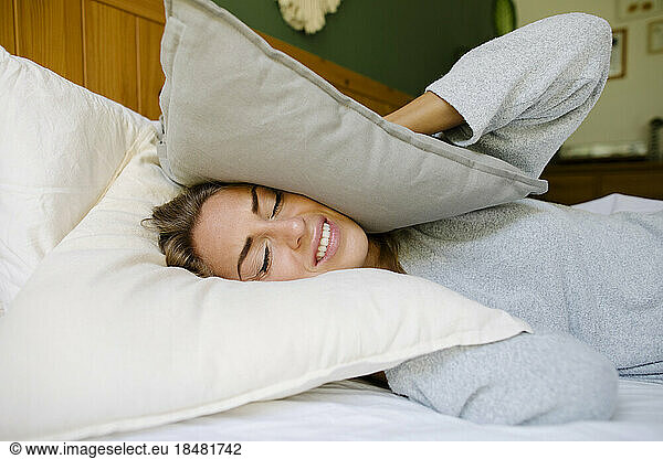 Woman closing ears with pillow in bed at home
