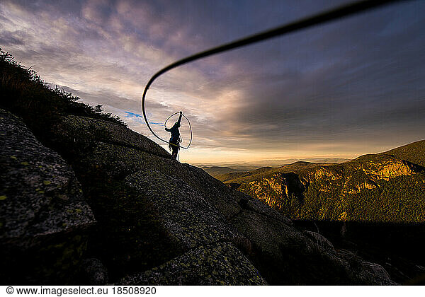 Woman coiling climbing rope at sunset on top of mountain