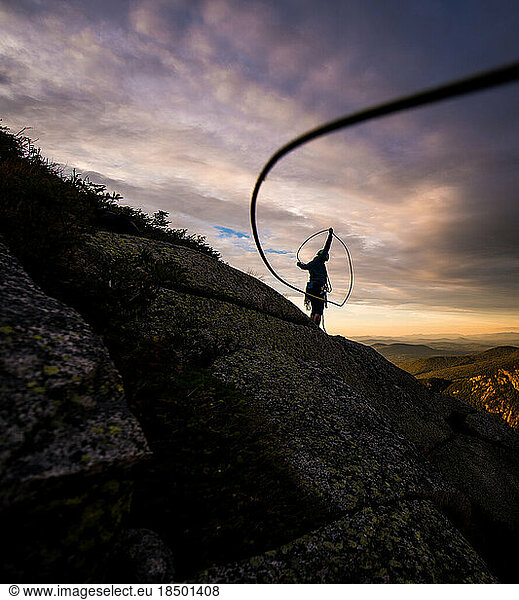 Woman coiling rock climbing rope at sunset on top of cliff