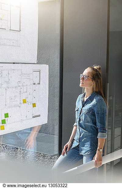 Woman contemplating plans on glass wall