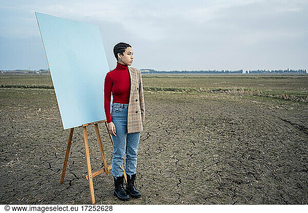 Woman contemplating while standing by painting on agricultural field