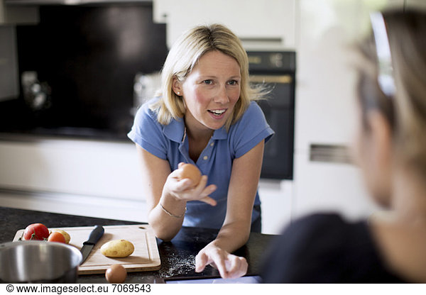 Woman conversing with friend while preparing food in kitchen