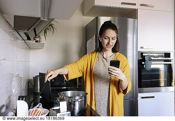 Woman cooking and having video call through smart phone in kitchen