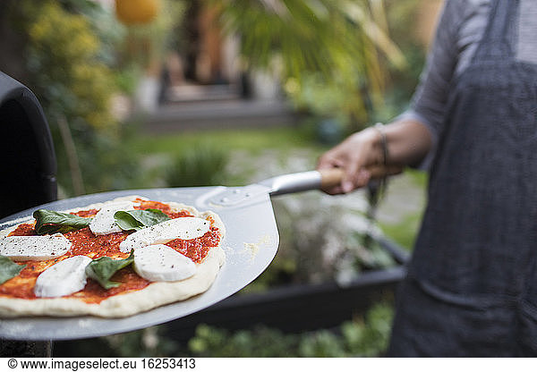 Woman cooking homemade pizza at pizza oven on patio