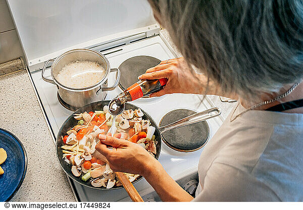 Woman cooks dinner in Asian style  adds oyster sauce to a frying pan