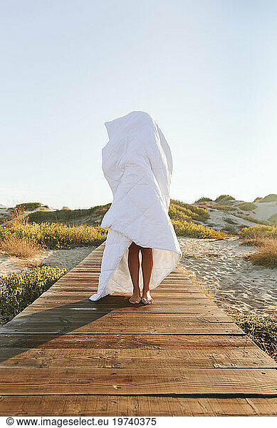 Woman covered in blanket standing on boardwalk at beach