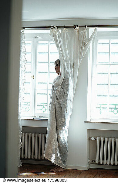 Woman covered in white curtain at home
