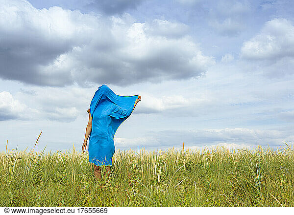 Woman covered with blue scarf standing at meadow
