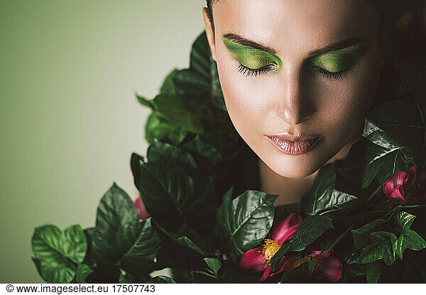 Woman covered with green plants against green background