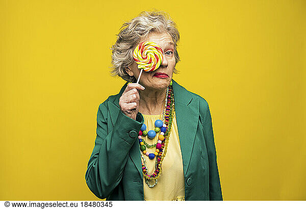 Woman covering eye with spiral candy against yellow background