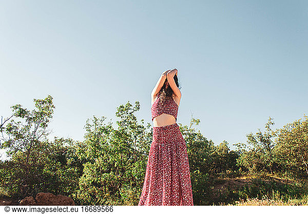 woman covering face with arms with long summer dress against blue sky