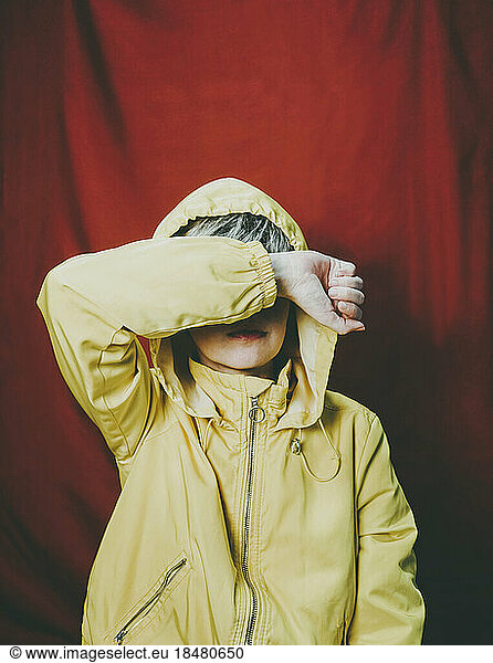 Woman covering face with hand standing against red backdrop