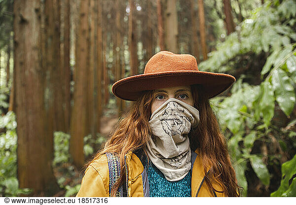 Woman covering face with scarf in forest