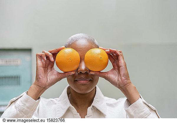 Woman covering her eyes with oranges outdoors