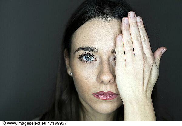 Woman covering one eye with hand in studio