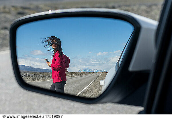 Woman crossing the route seen through side-view mirror of car