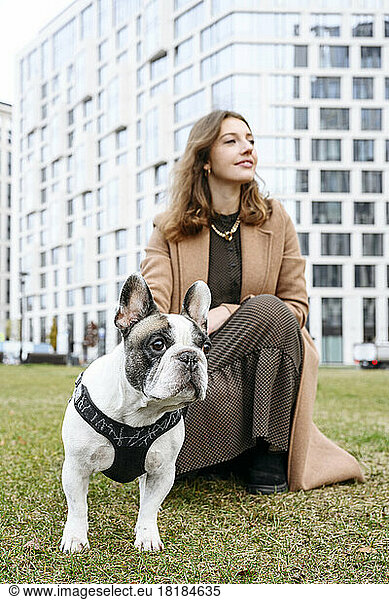 Woman crouching with French bulldog in front of building