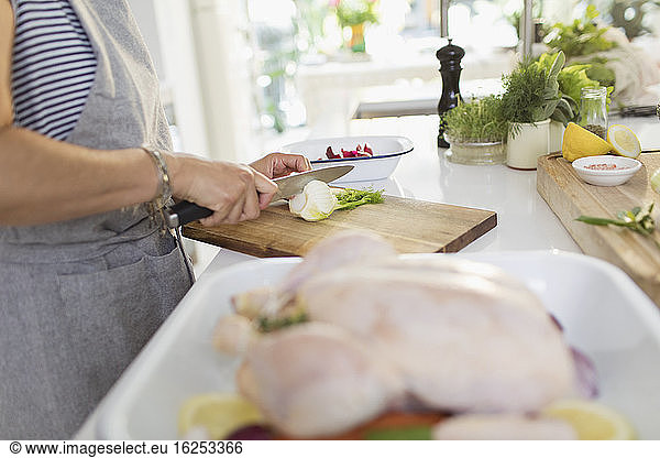 Woman cutting herbs for chicken dish in kitchen