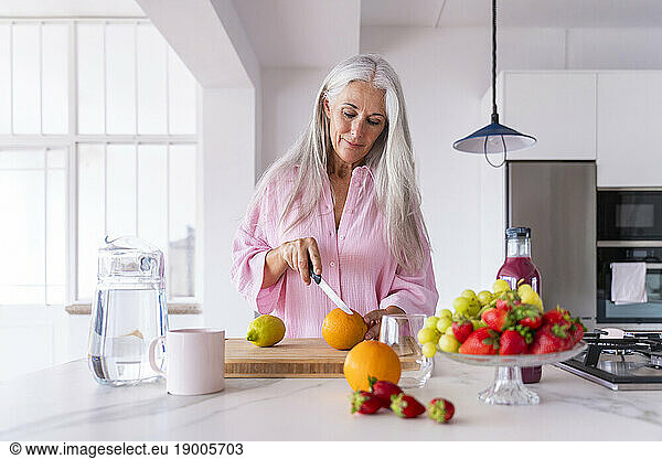 Woman cutting orange in kitchen at home