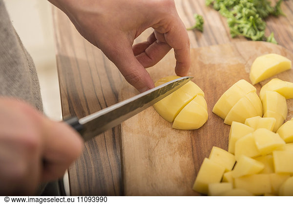 Woman cutting potatoes on cutting board in kitchen
