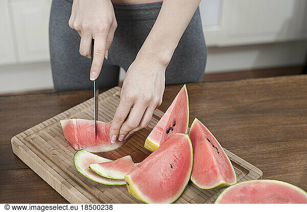 Woman cutting slices of watermelon in the kitchen  Bavaria  Germany