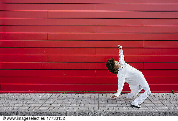 Woman dancing on footpath by red wall