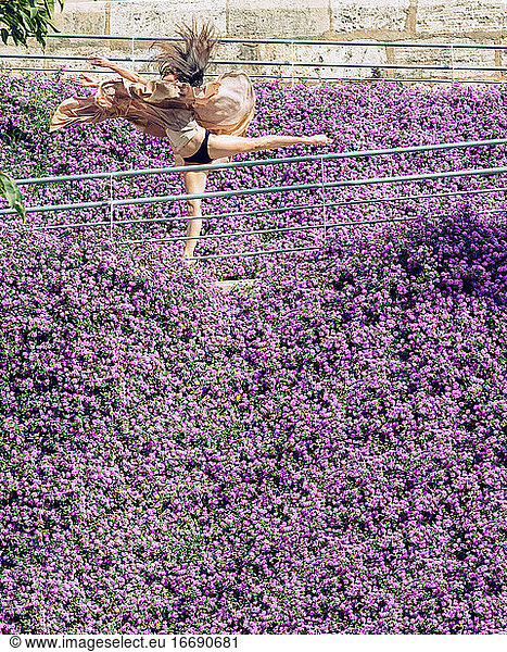 Woman dancing surrounded by purple flowers with a flying dress