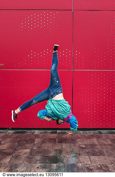 Woman doing cartwheel on street against red wall